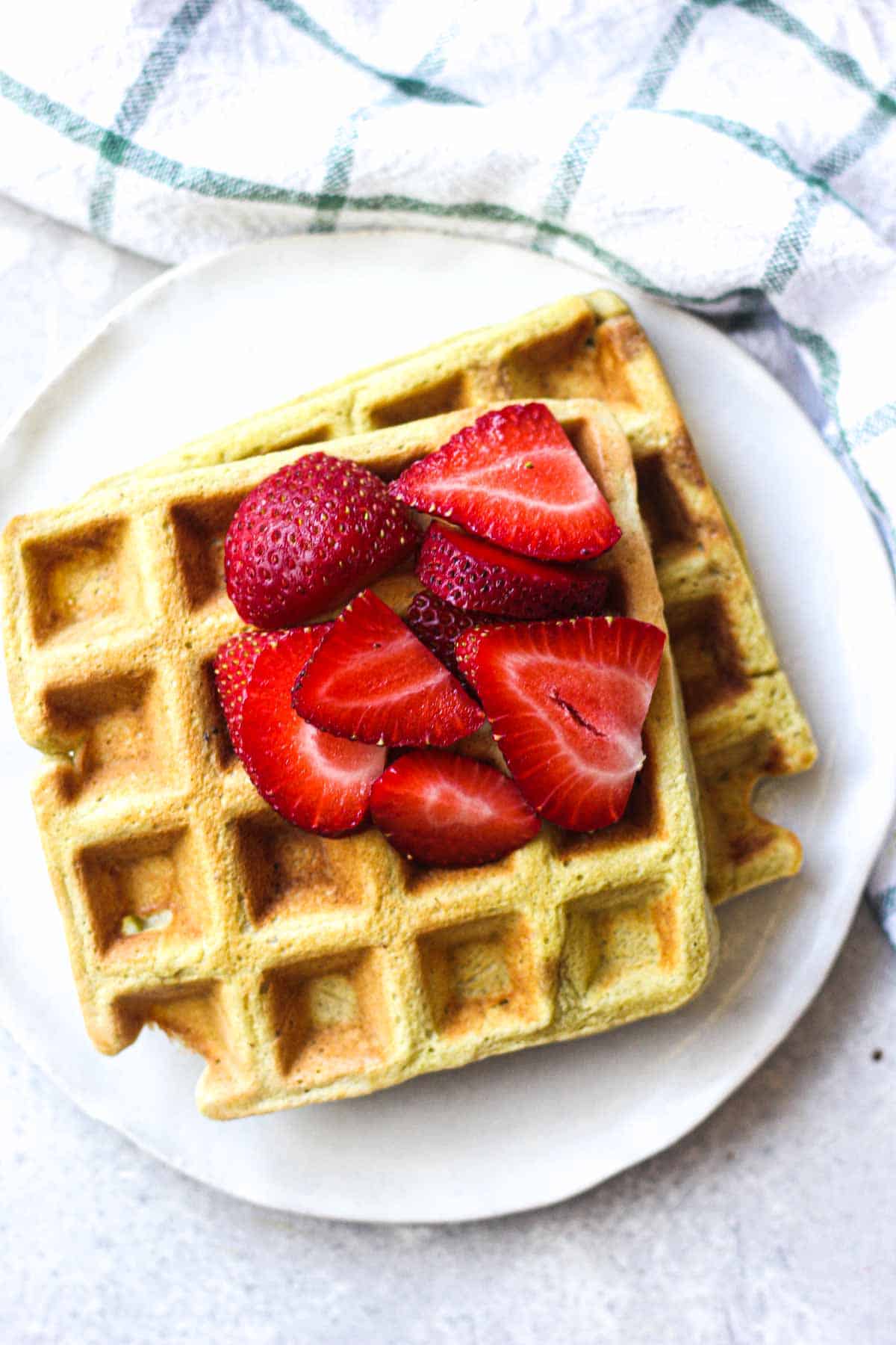 two waffles on a plate with sliced strawberries on top