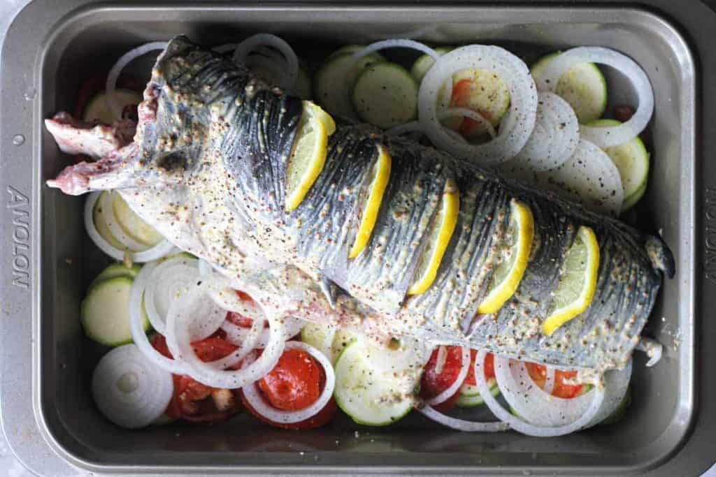  poisson-chat entier sur des légumes tranchés dans la plaque de cuisson 