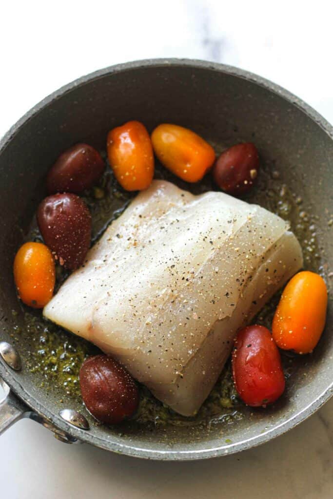 seasoned raw barramundi fillet in a pan with cherry tomatoes before cooking