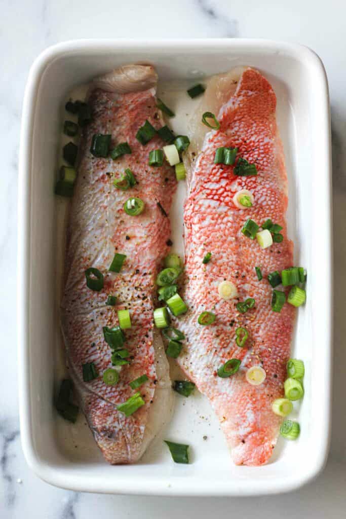 raw ocean perch with green onions on top before baking