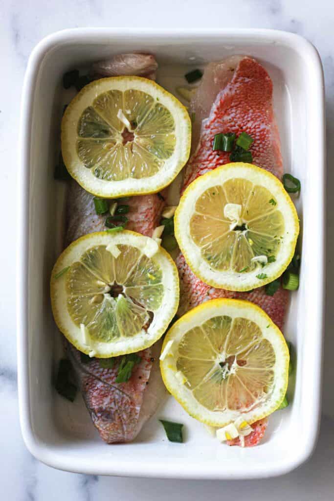  filetes de perca oceánica con rodajas de limón en una fuente para hornear blanca