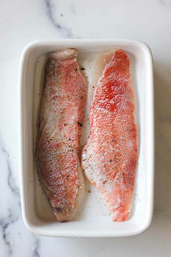 piel cruda en filetes de perca marina en una fuente blanca para hornear