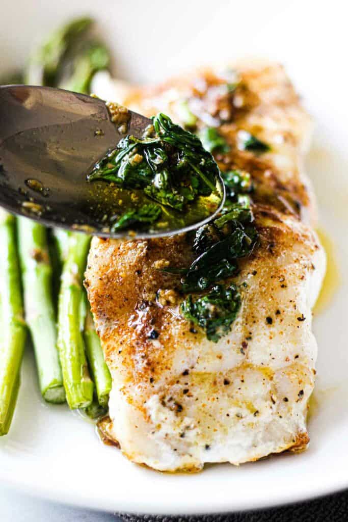 grouper with asparagus on a white plate topped with cilantro butter