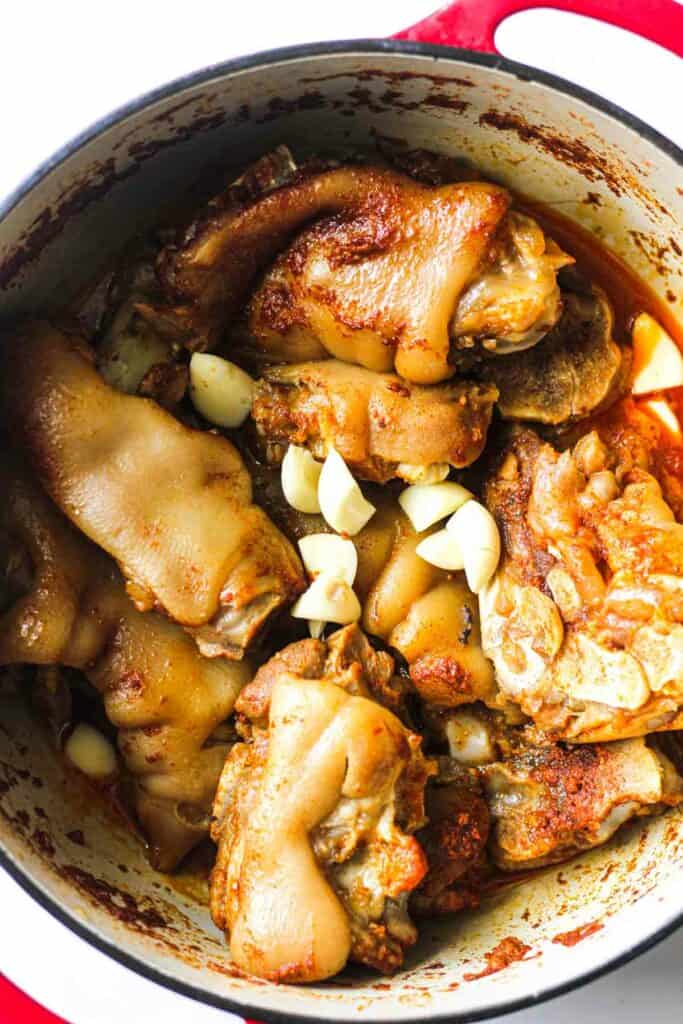 halfway through cooking meat in the pot with garlic on top