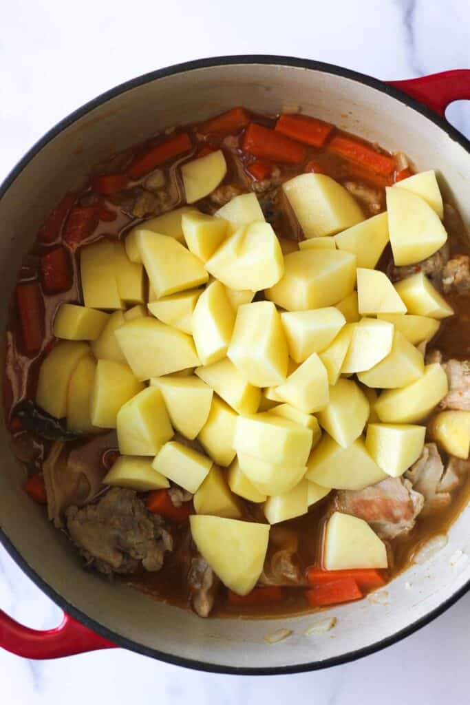 peeles and cubed yellow potatoes in a pot with braised rabbit