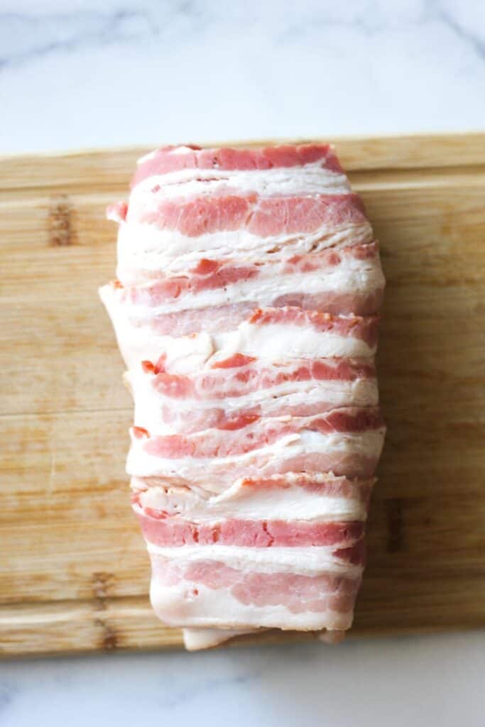 raw bacon wrapped tenderloin on a wooden board