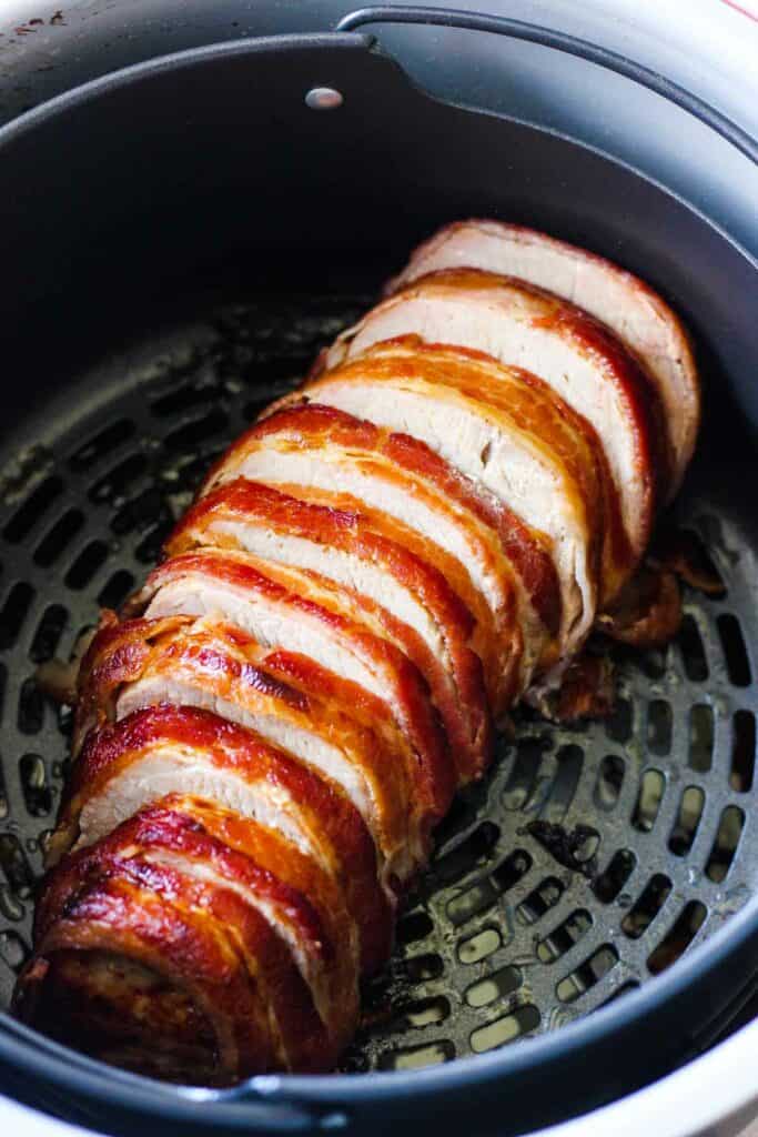 sliced tenderloin in air fryer basket with crispy bacon on top