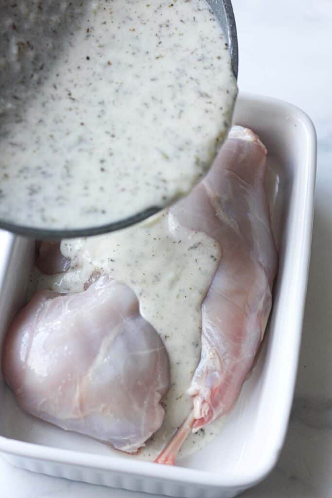 raw rabbit legs with souce pouring from the grey pan
