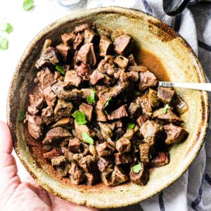 beef heart stew in a brown bowl with chopped parsley on top
