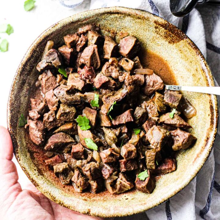 beef heart stew in a brown bowl with chopped parsley on top
