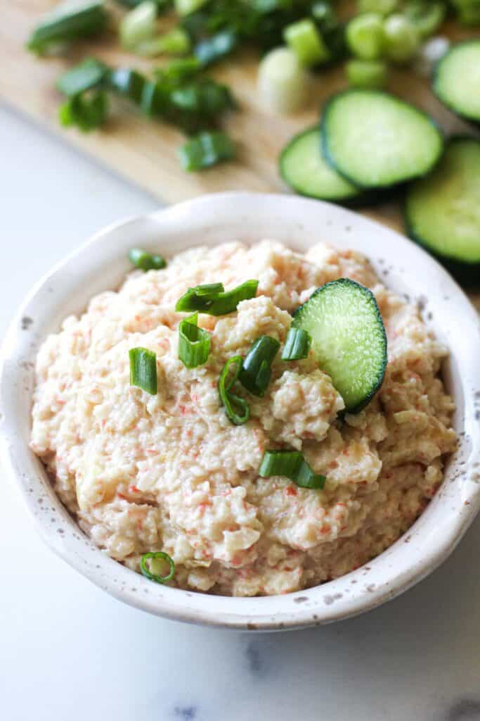 crab dip in white bowl with cucumber and chopped scallions