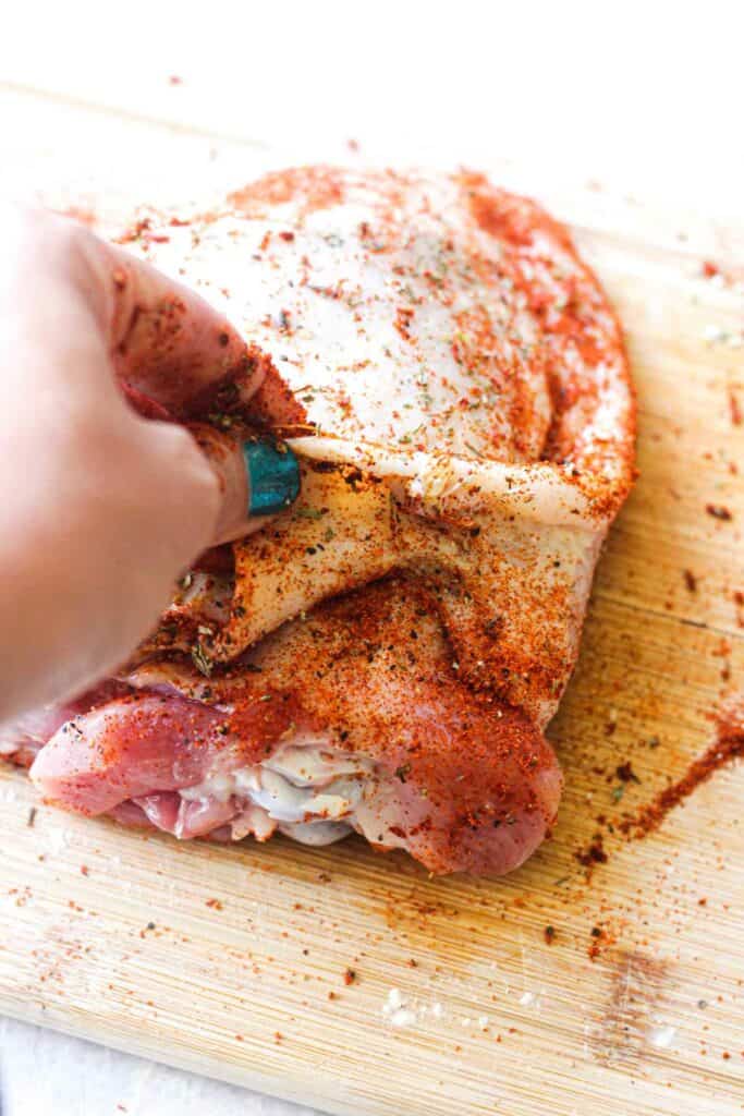 raw turkey thigh covered in spices on a brown cutting board