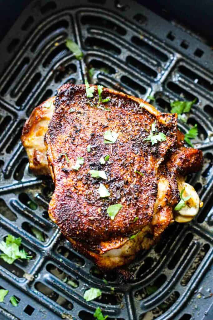 cooked crispy turkey thigh in the black air fryer basket with chopped cilantro on top