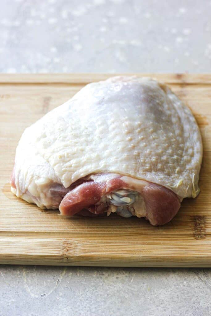 raw bird thigh on a cutting board with skin on