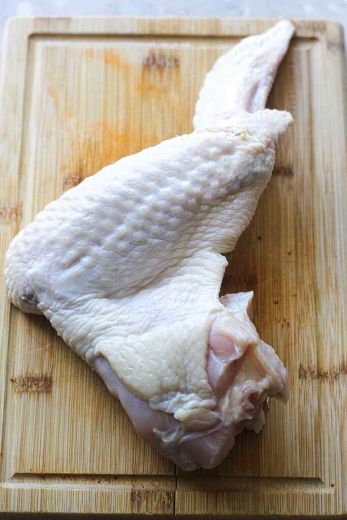 raw whole turkey wing on a brown cutting board