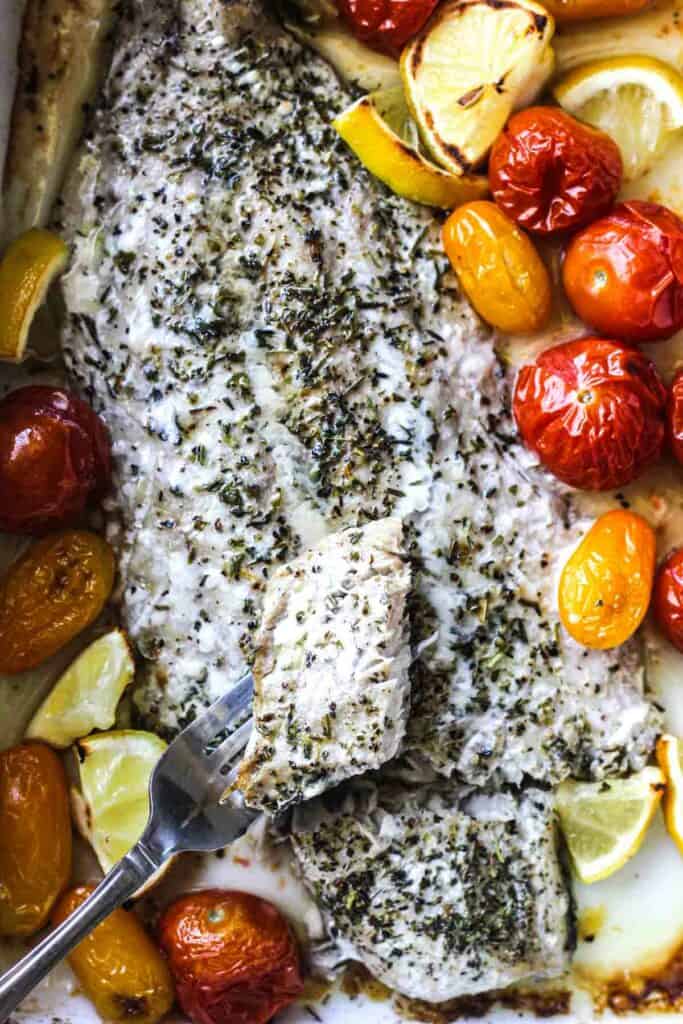 a piece of baked white fish on a fork with herbs on it