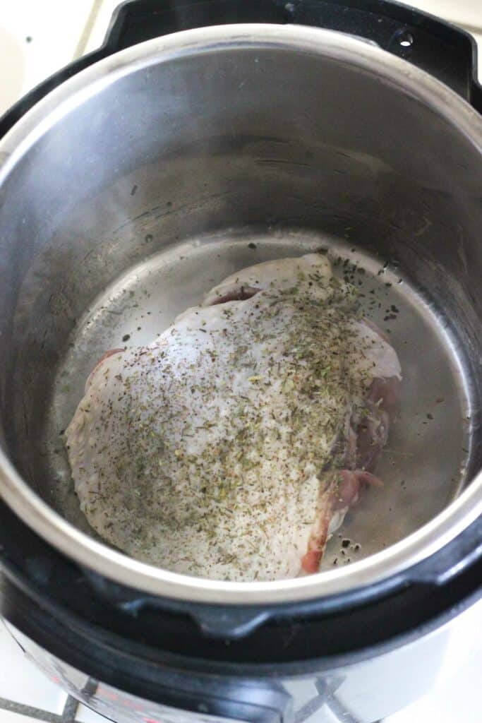 raw turkey thigh in instant pot iner pot covered in spices