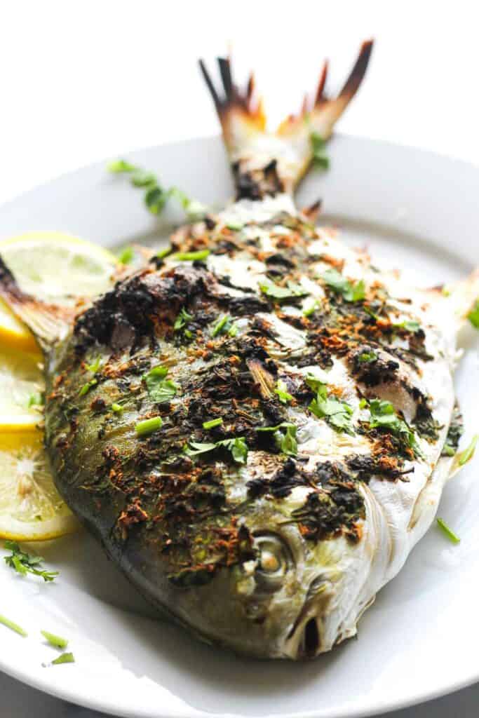 baked whole golden pompano on the plate with lemon