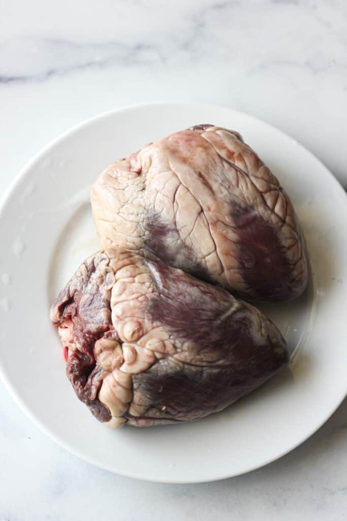 2 raw whole lamb hearts on the white plate