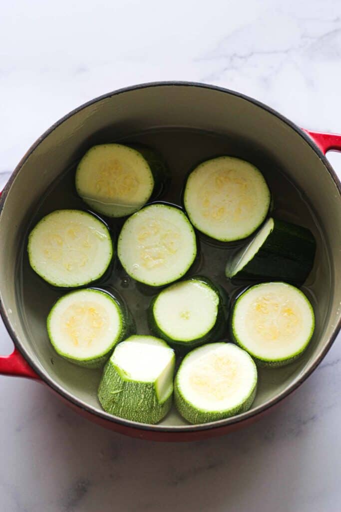raw zucchini chunks in red pot with water bafore boiling