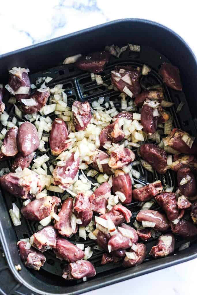raw chicken hearts with onions in the air fryer basket