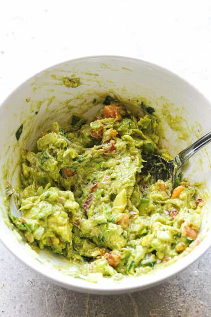 mixing ingredients for the avocado dip in a white bowl with a spoon