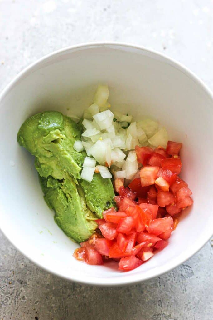 scooped avocado , chopped tomatoes and chopped onions in a bowl
