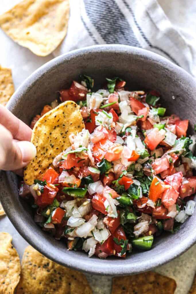 crab pico de gallo in a small serving bowl with a tortilla chip in hand