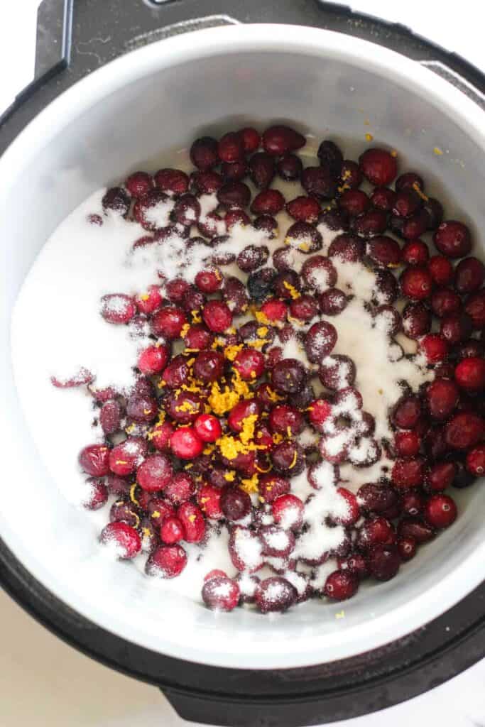 frozen cranberries in the inner pot with white sugar and orange peel on top