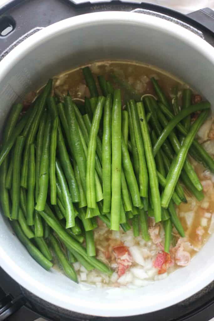 raw green beans sitting on top of bacon and chopped onions in the pressure cooker pot
