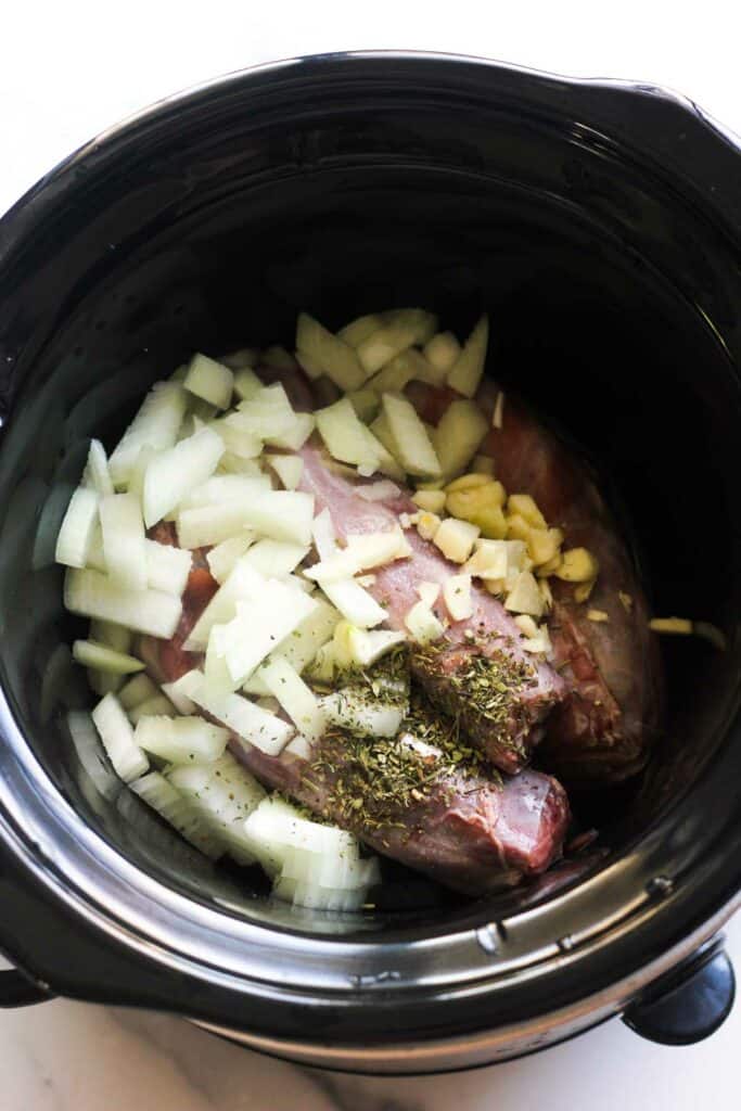 chopped onion, garlic and dried spices on top of meat in crock pot