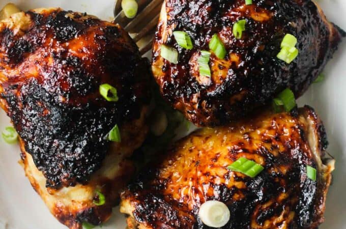 bbq chicken thighs on a white plate with chopped green onions