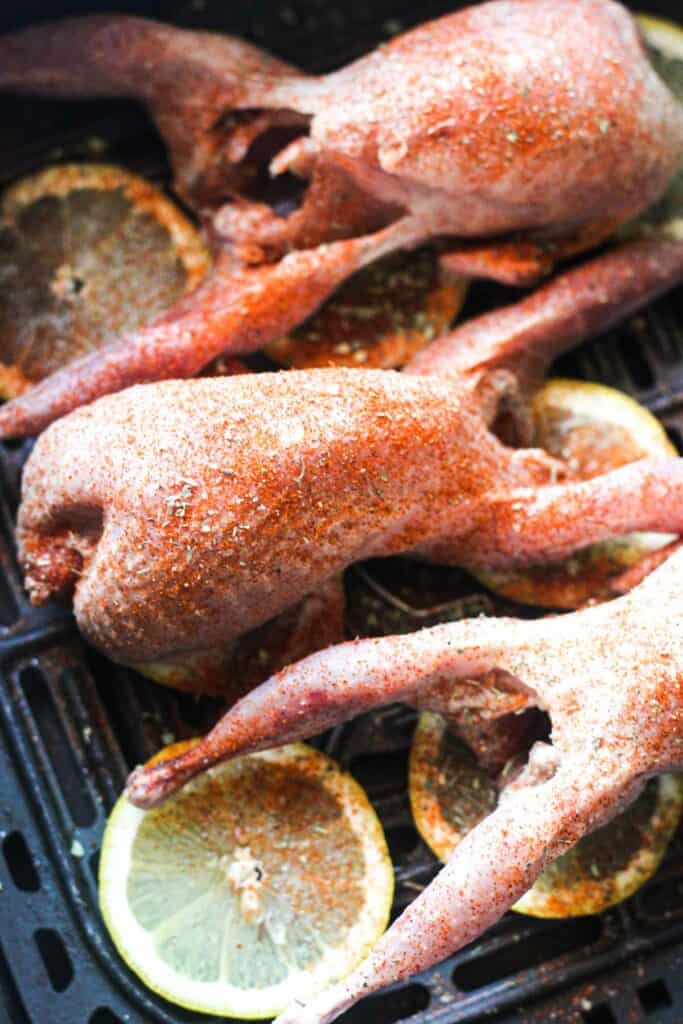 raw quails with seasoning and lemon in the air fryer basket