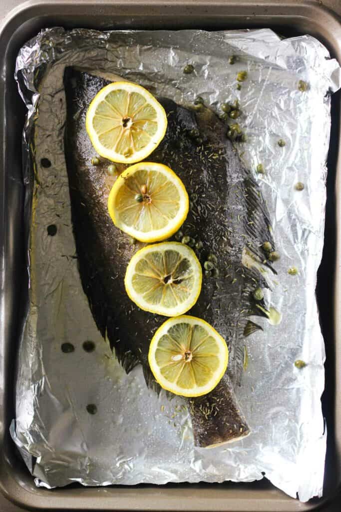 raw whole fish with lemon and thym eand capers on the baking dish with foil