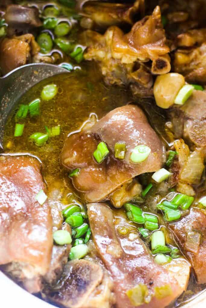 cooked pig feet in crock pot with chopped green onions on top