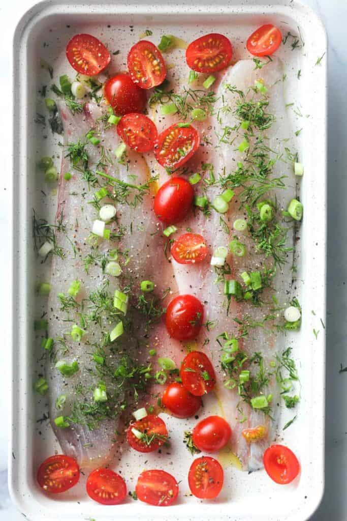 raw fish fillets with cherry tomatoes, dill and chopped green onions on top
