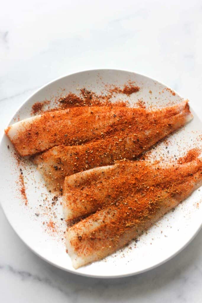 heavily seasoned raw sole fish on the white plate