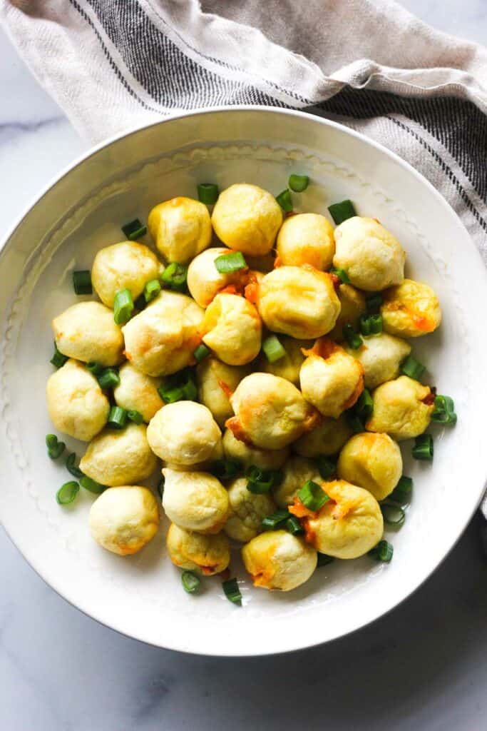 little yellow stuffed gnocchi with chopped green onions on a white plate