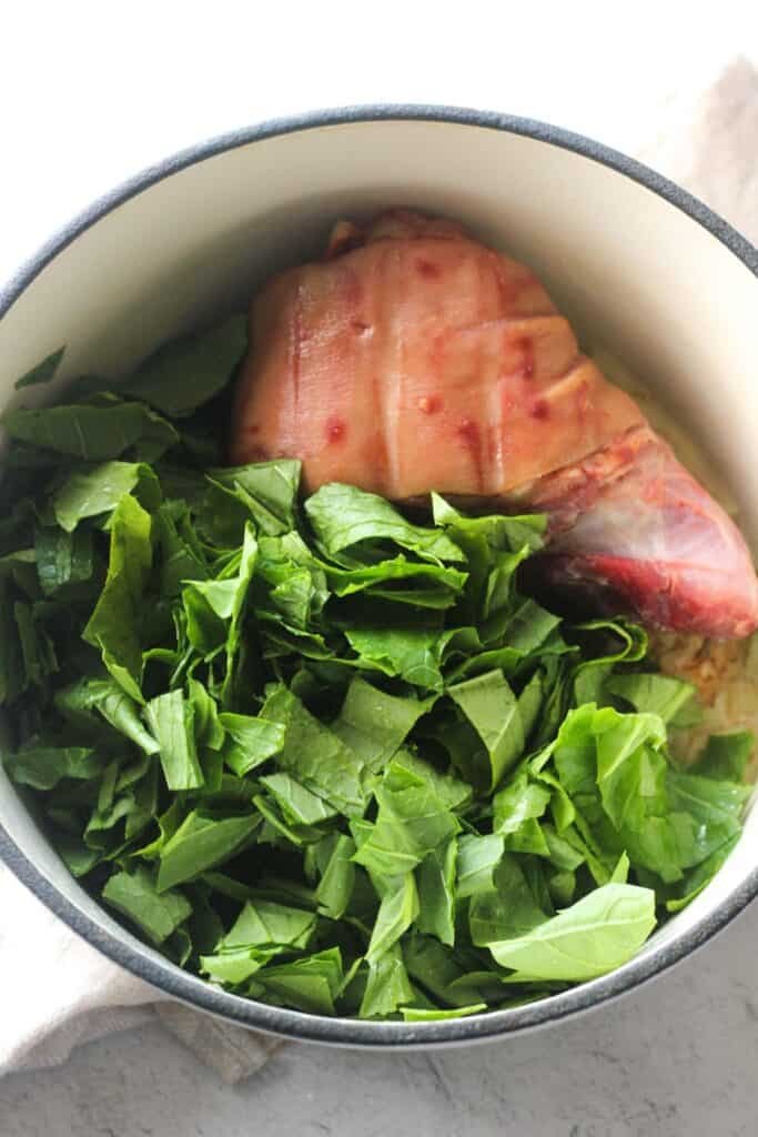 greens with ham hock in a white pot before cooking