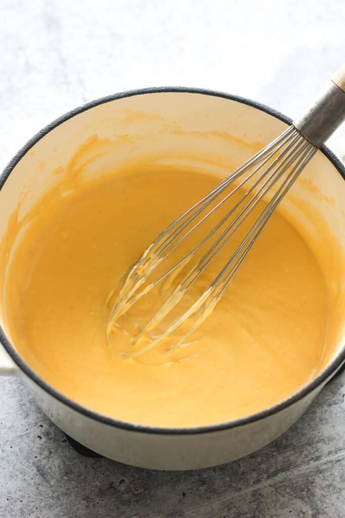 cheese sauce in the white pot with whisk
