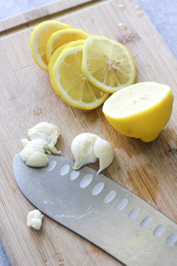 smashed garlic and sliced lemon on the brown cutting board