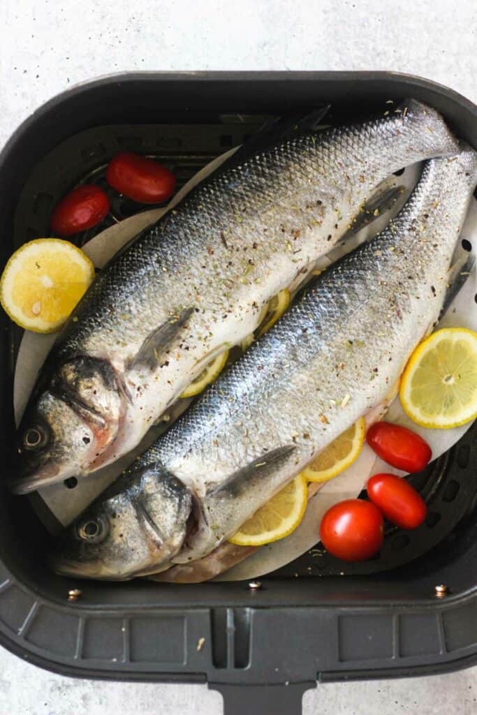 two raw branzino fish in the air fryer before cooking