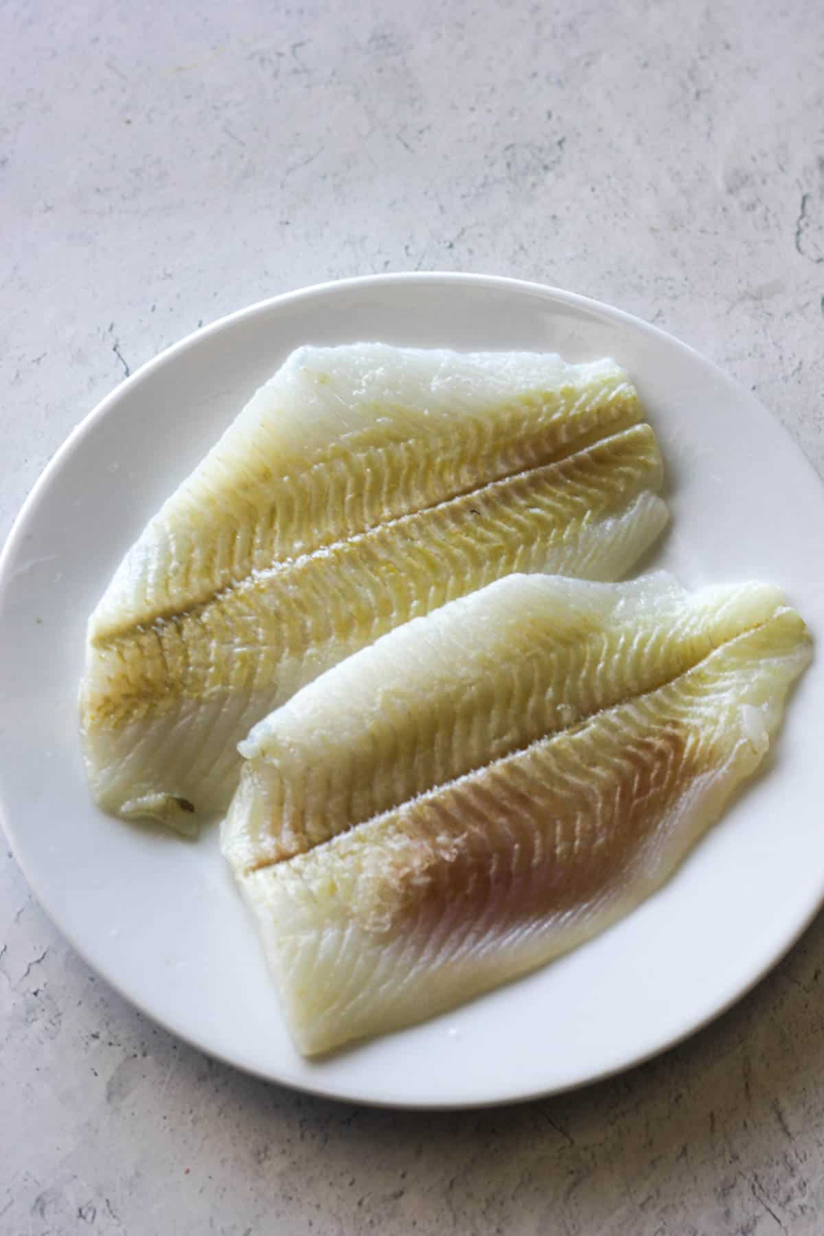 raw flounder fillets on the white plate