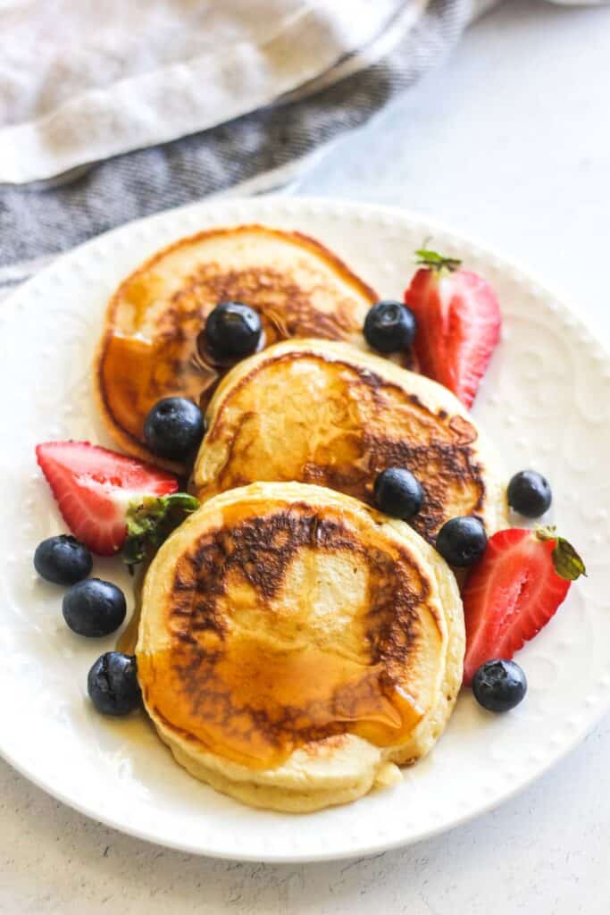 fluffy pancakes with evaporated milk on the white plate with maple syrup and berries