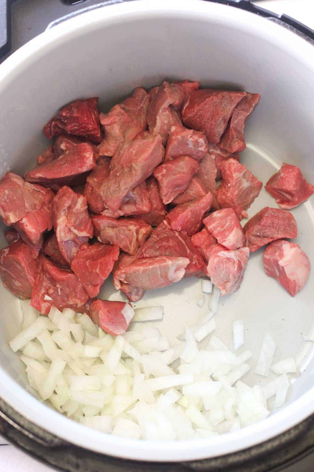 cubed beef and chopped onion in pressure cooker inner pot