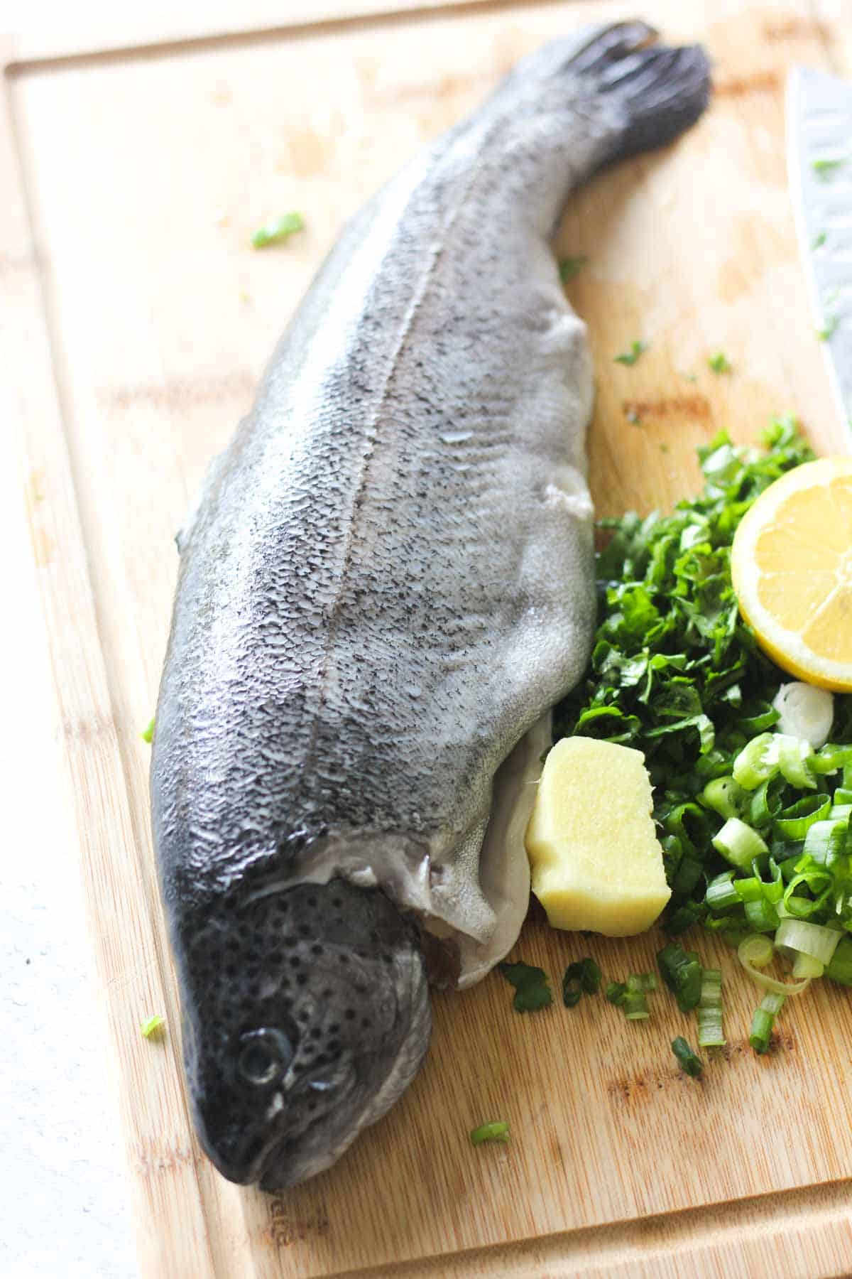 raw white fish with chopped green onions and ginger on the brown cutting board