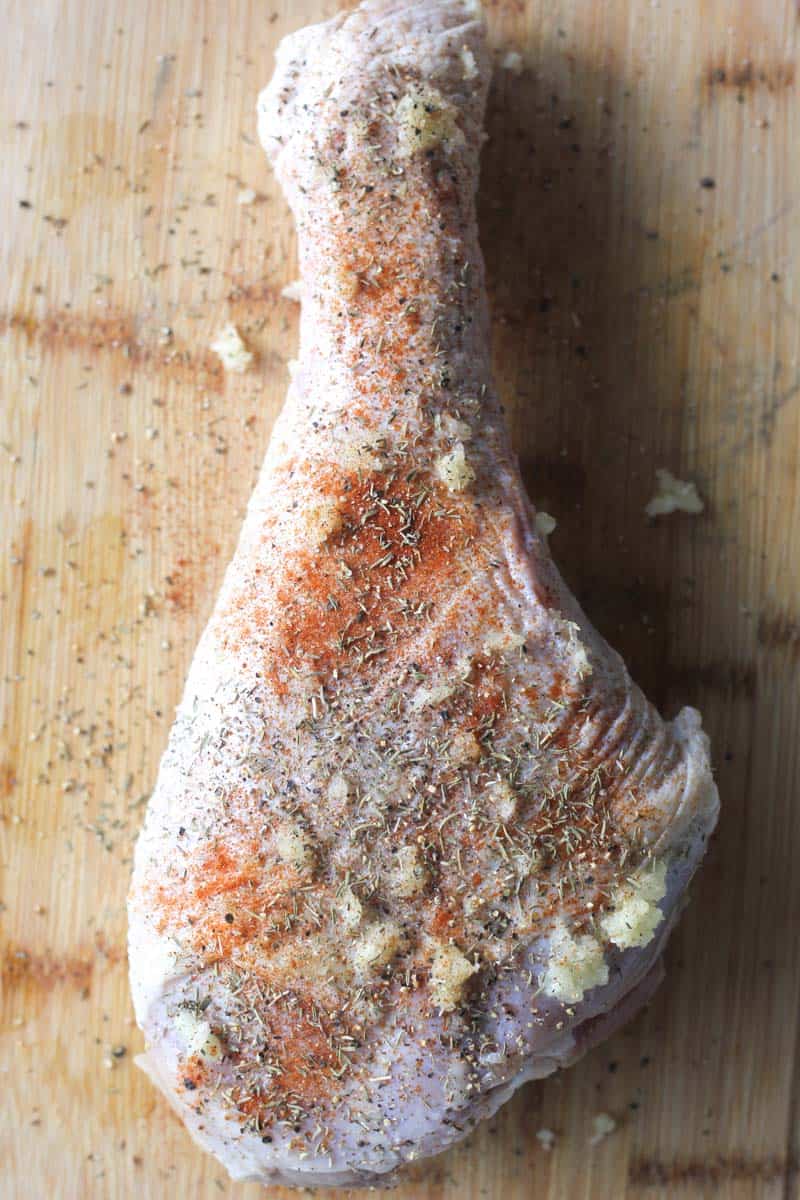 raw turkey leg covered in spices and minced garlic