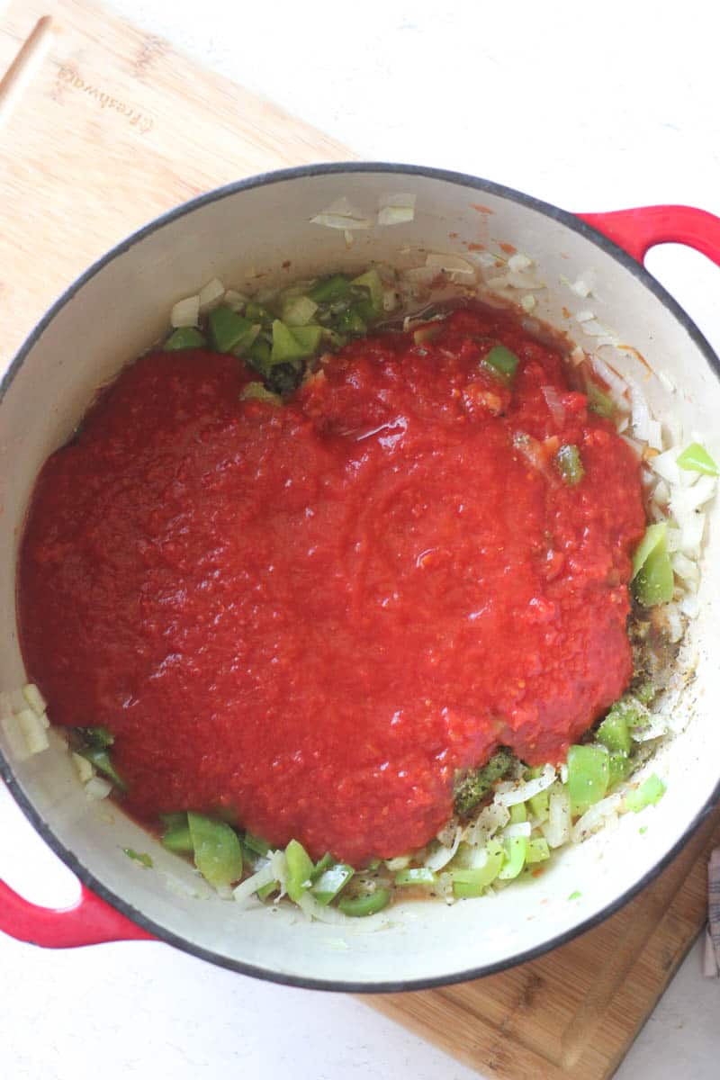 adding crushed tomatoes to chopped green bell peppers and onions