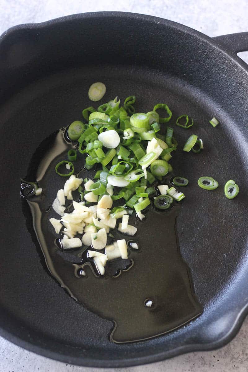 adding garlic and chopped green onions to the pan with oil