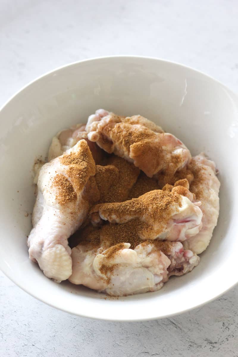 adding cajun seasoning to raw chicken wings in the bowl